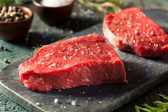 A bright red cut of raw beef on a cutting board with seasonings. 