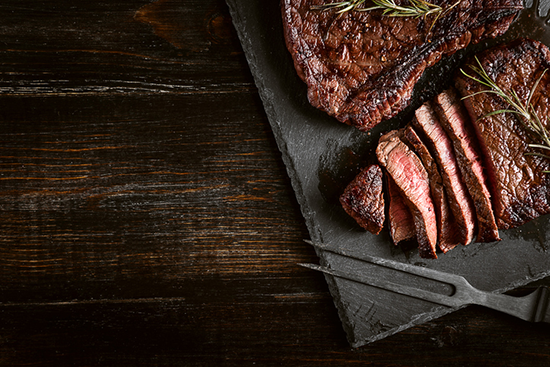 A cooked and sliced delicious steak on a cutting board on a wooden background. 