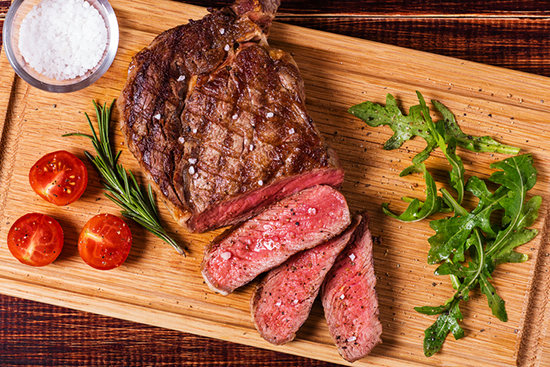 A grilled and sliced ribeye steak with tomatoes, salt, and arugula.