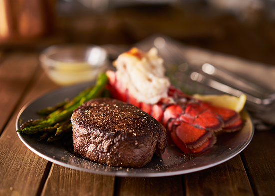 A surf and turf filet steak dinner plate with asparagus on a wooden table. 