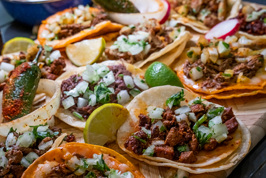 A group of steak street tacos with onions and lime wedges. 