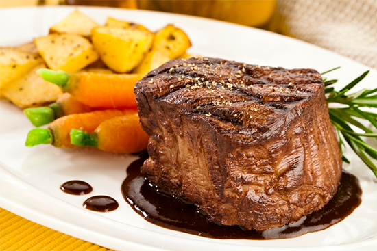 Cooked beef tenderloin steak on a plate with potatoes and carrots.