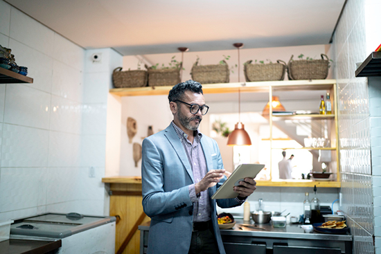 A man using a tablet in a professional kitchen. 