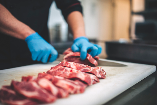 A person hand-cutting individual steaks from a whole sub-primal piece of meat on a white cutting board.