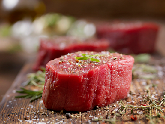 An uncooked filet mignon steak with seasonings on a cutting board. 